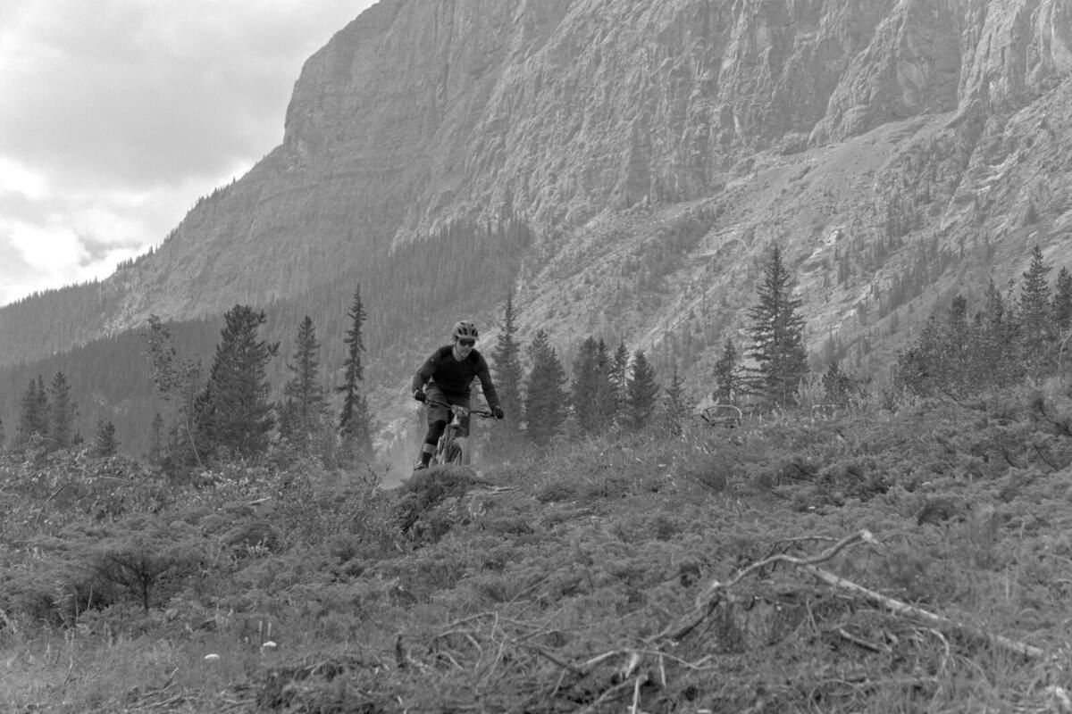 mountain biker riding below a large rock face, black and white